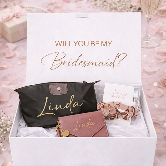 Gift set with 'Will You Be My Bridesmaid?' card, black pouch, pink wallet, and scrunchie in a box.