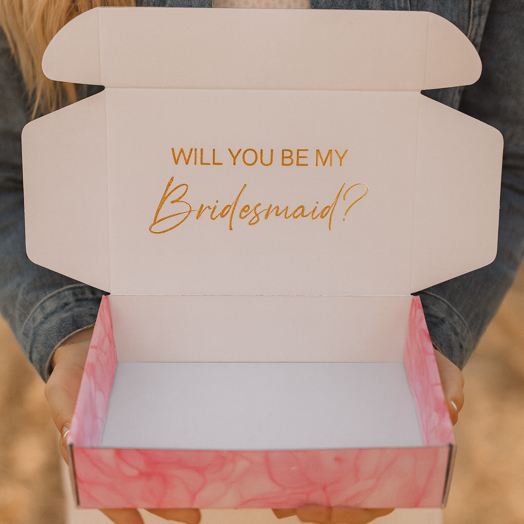 Person holding a box with 'Will You Be My Bridesmaid?' text.