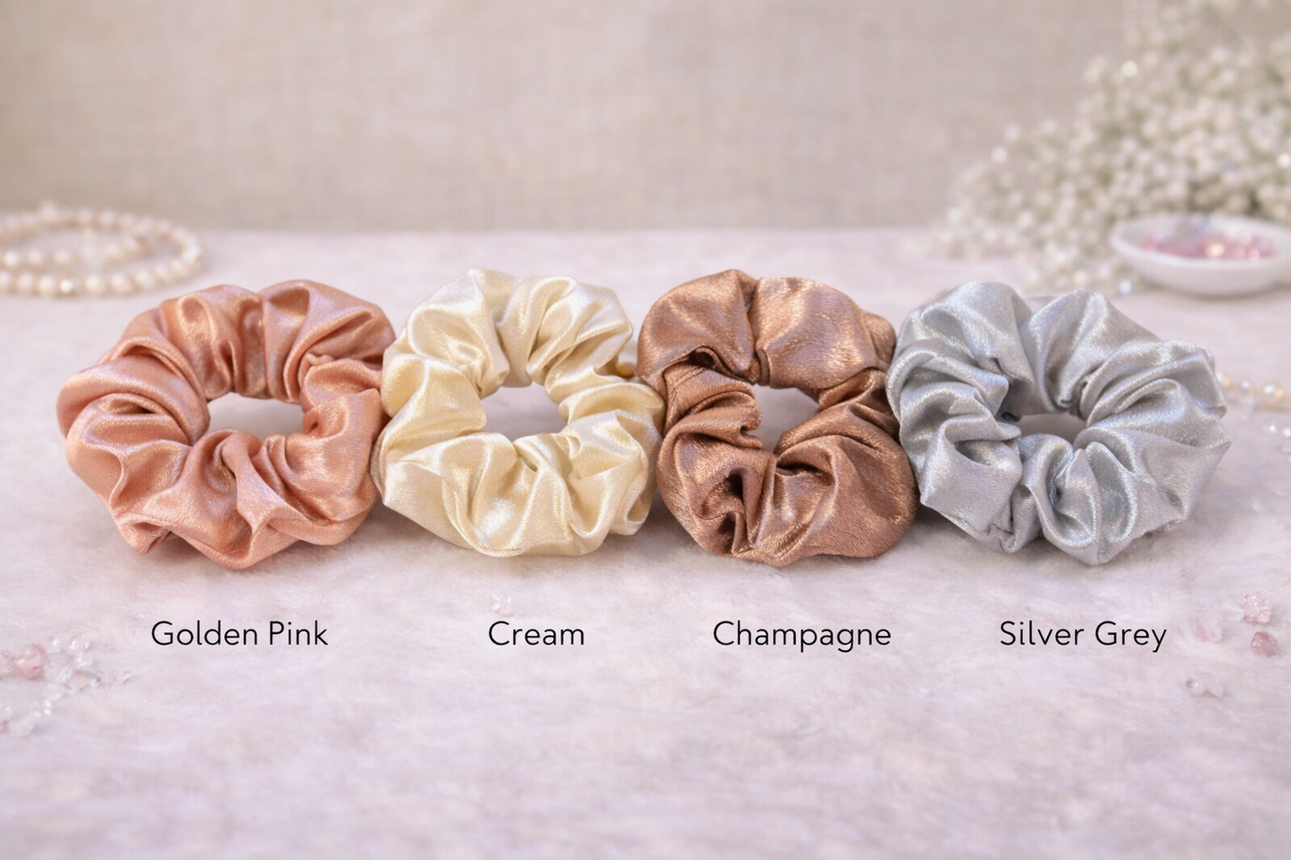 Four scrunchies in different colors on a textured surface with labels underneath.