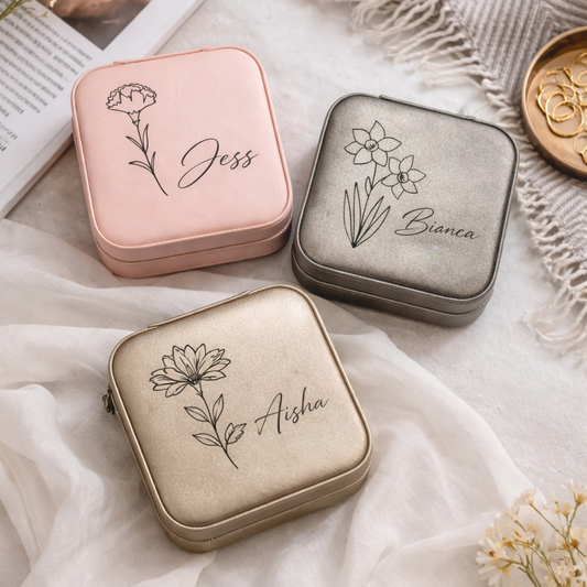 Three small jewelry cases with floral designs and names on a soft fabric background