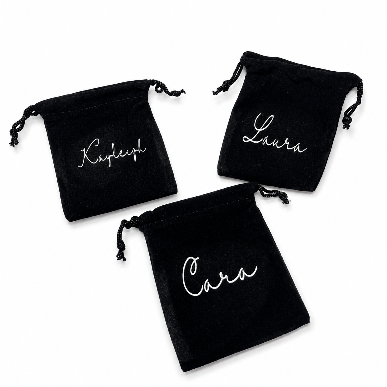 Three black drawstring bags with names 'Kemble', 'Laura', and 'Cara' embroidered on them.