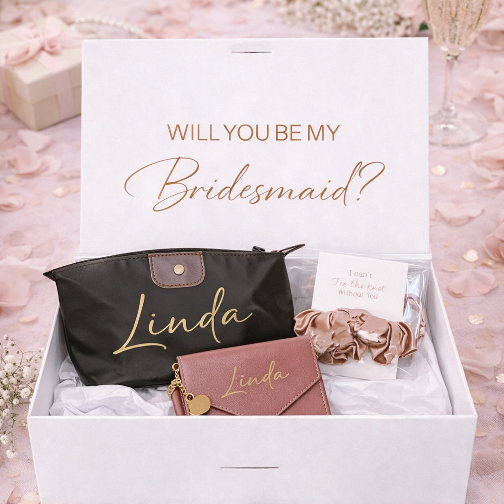 Gift set with 'Will You Be My Bridesmaid?' card, black pouch, pink wallet, and scrunchie in a box.