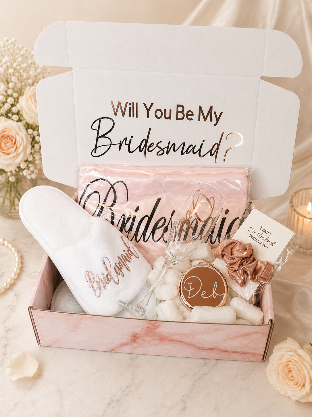 Gift box with 'Will You Be My Bridesmaid?' message and personalized items on a floral background.