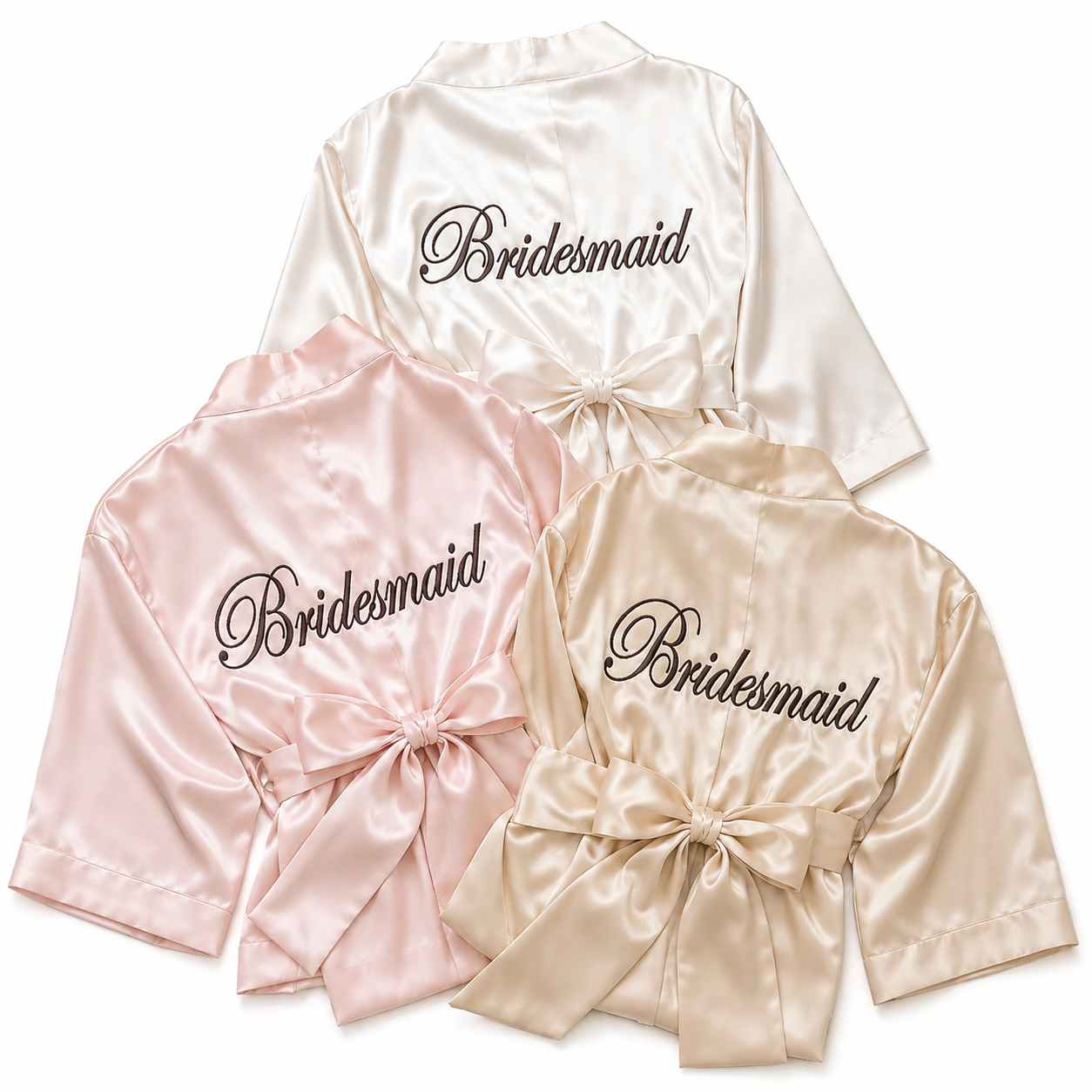 Three satin robes in pink, white, and beige with 'Bridesmaid' embroidery on a white background.