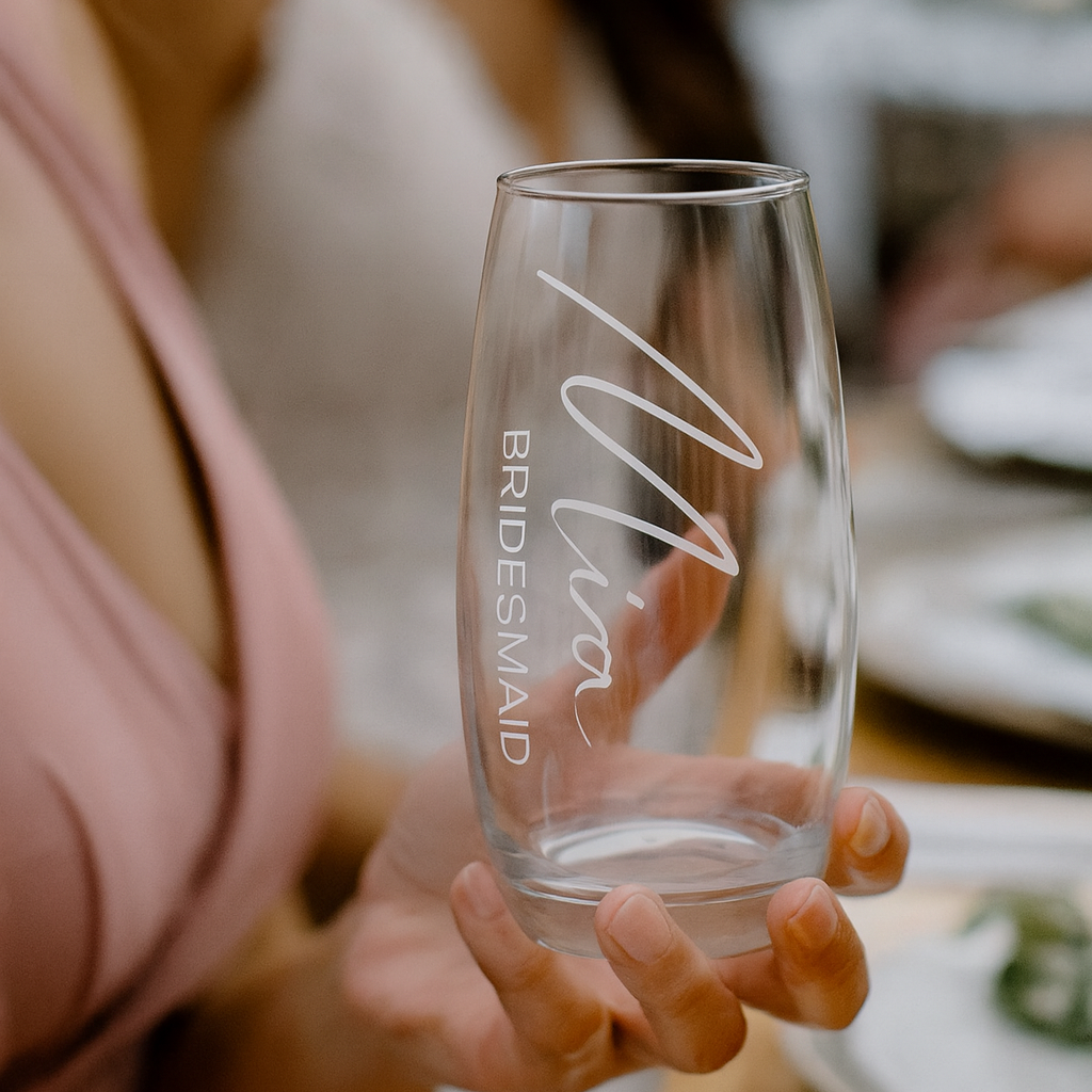 Clear glass with 'Bridesmaid' and 'Mia' engraved, held by a person.