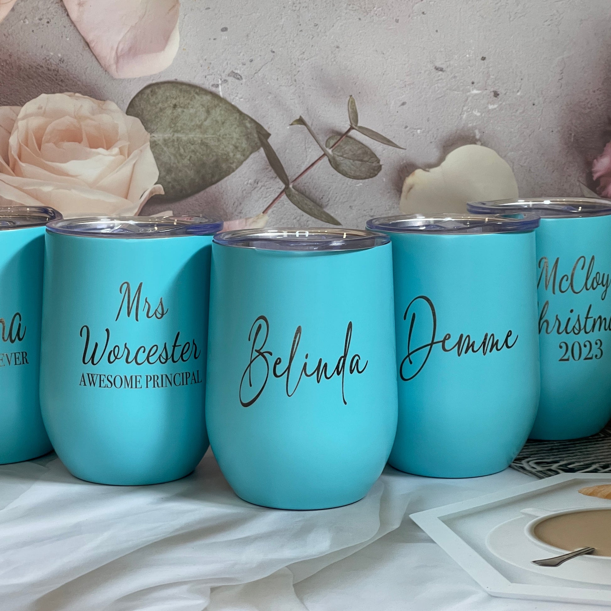 A set of engraved reusable travel wine tumblers in blue color, with personalized names engraved on each.