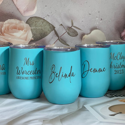 A set of engraved reusable travel wine tumblers in blue color, with personalized names engraved on each.