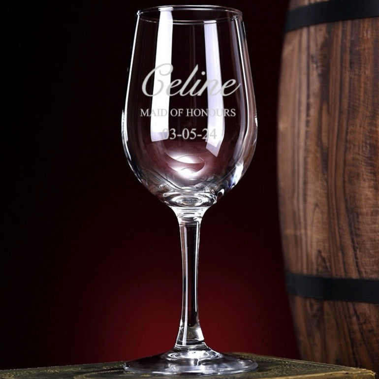A clear glass wine glass with engraved text on the stem, displayed against a wooden background.