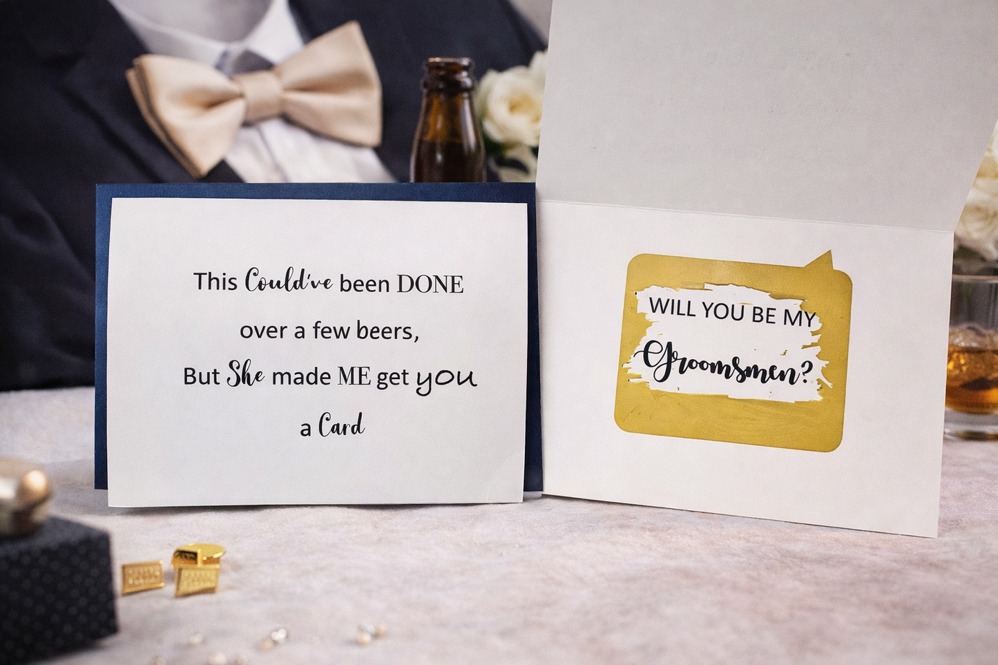 Groomsmen proposal card with humorous text and gold accents on a table with drinks and cufflinks.