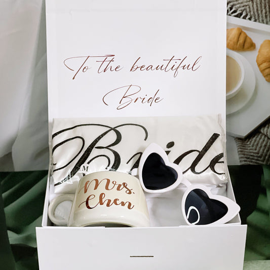 A gift box for the bride opened to display a white mug with 'Bride' written in a decorative font, a pair of sunglasses with 'Mr. Chan' inscribed on the arms, and a personalized text that reads 'To the beautiful Bride'.