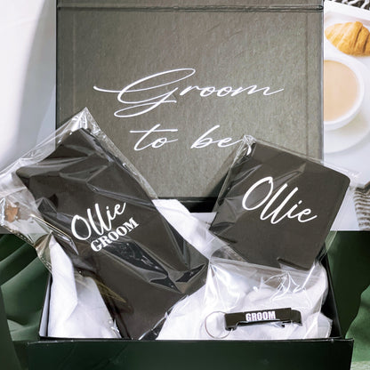 A black gift box with 'Groom to be' text in white, containing personalized items for the groom, sealed with a white ribbon.
