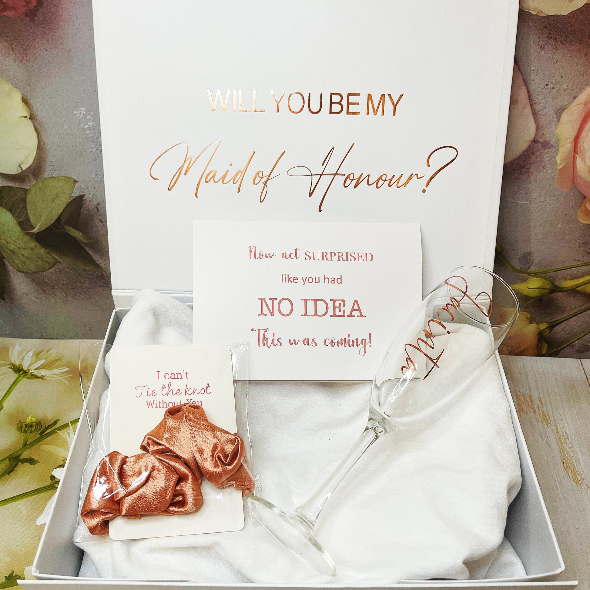 A gift box proposal set for bridesmaids including a personalized box with text, a champagne flute, a silk ribbon, and a card with the question 'Will you be my Maid of Honour?'.