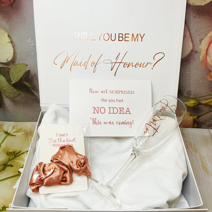 A gift box proposal set for bridesmaids including a personalized box with text, a champagne flute, a silk ribbon, and a card with the question 'Will you be my Maid of Honour?'.