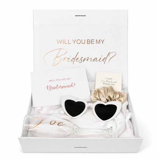 Gift set with heart-shaped sunglasses, bow, and card in a box asking 'Will you be my bridesmaid?'
