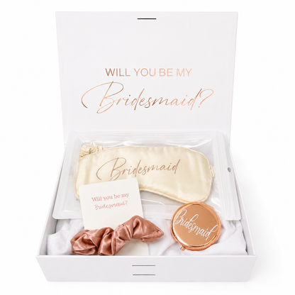 Gift set with 'Will you be my bridesmaid?' items including a sleep mask, hair tie, and compact mirror in a box.