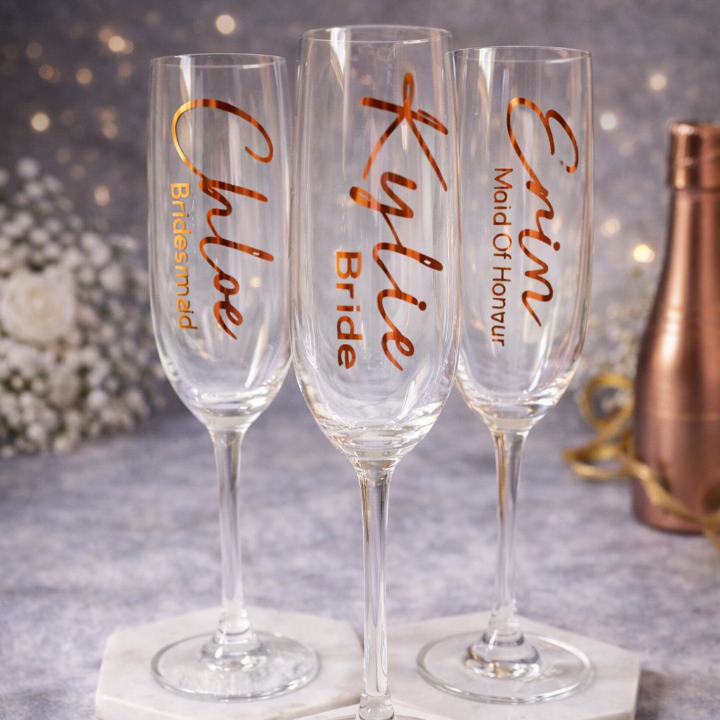 Three champagne flutes with personalized names on a gray surface with decorative items.