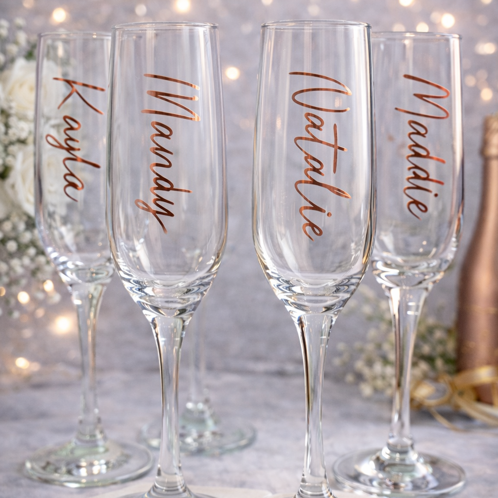 Set of four personalized champagne flutes with names on a decorative surface.