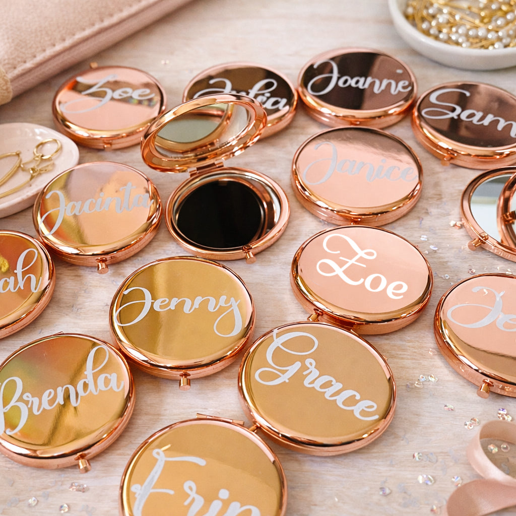 Compact mirrors with names engraved on their lids arranged on a surface.
