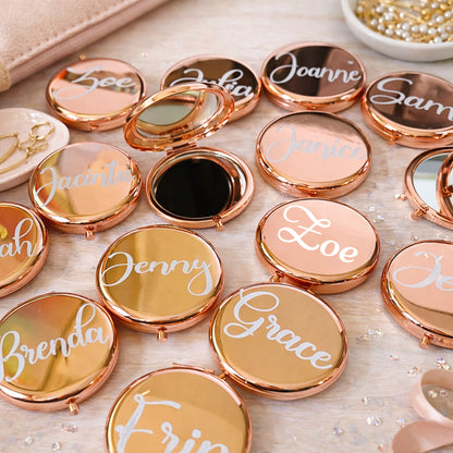 Compact mirrors with names engraved on their lids arranged on a surface.