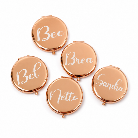 Set of five rose gold compact mirrors with names engraved on them against a white background