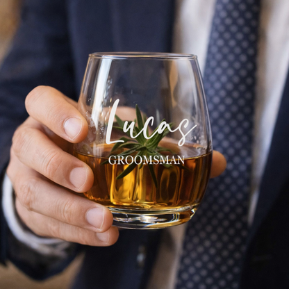Hand holding a glass of whiskey with 'Lucas Groomsman' engraving