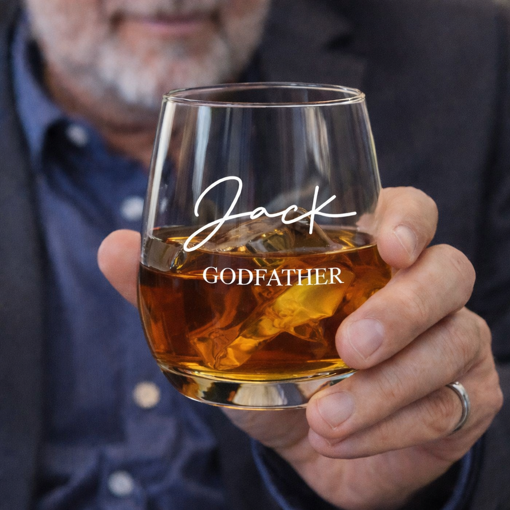 Person holding a glass of whiskey with 'Jack GODFATHER' engraving.