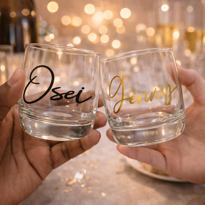 Two hands holding personalized glass tumblers with 'Osei' and 'Jenny' on a blurred background.
