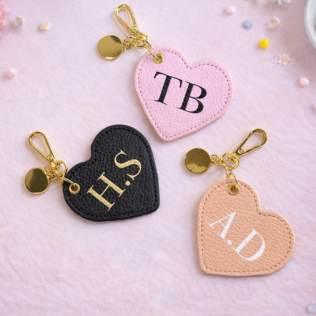 Heart-shaped keychains with initials on a pink surface with decorative elements.