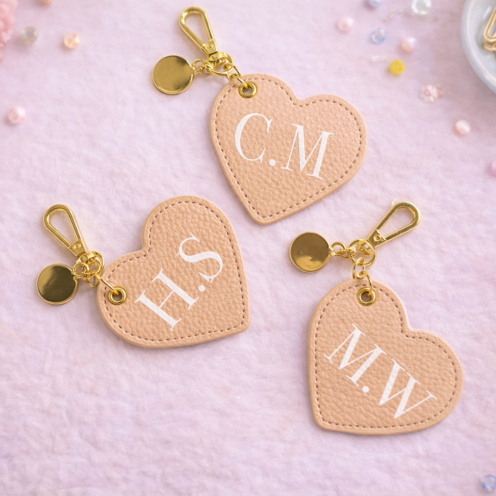 Heart-shaped keychains with initials on a pink surface with decorative items.