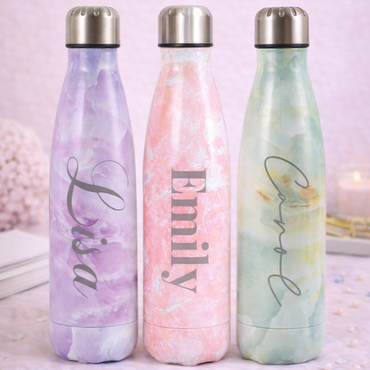 Three marbled water bottles with names 'Lisa', 'Emily', and 'Coral' on a light pink background.