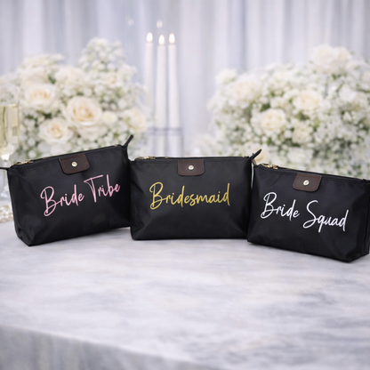 Black makeup bags with 'Bride Tribe', 'Bridesmaid', and 'Bride Squad' text on a table with floral decorations.