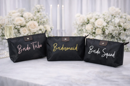 Black cosmetic bags with 'Bride Tribe', 'Bridesmaid', and 'Bride Squad' text on a table with floral decorations.