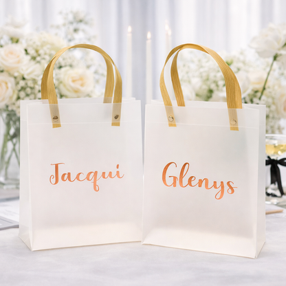 Two white gift bags with 'Jacqui' and 'Glenys' text, wooden handles, on a blurred floral background.
