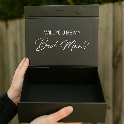 Black box with 'Will You Be My Best Man?' text held by a person outdoors.