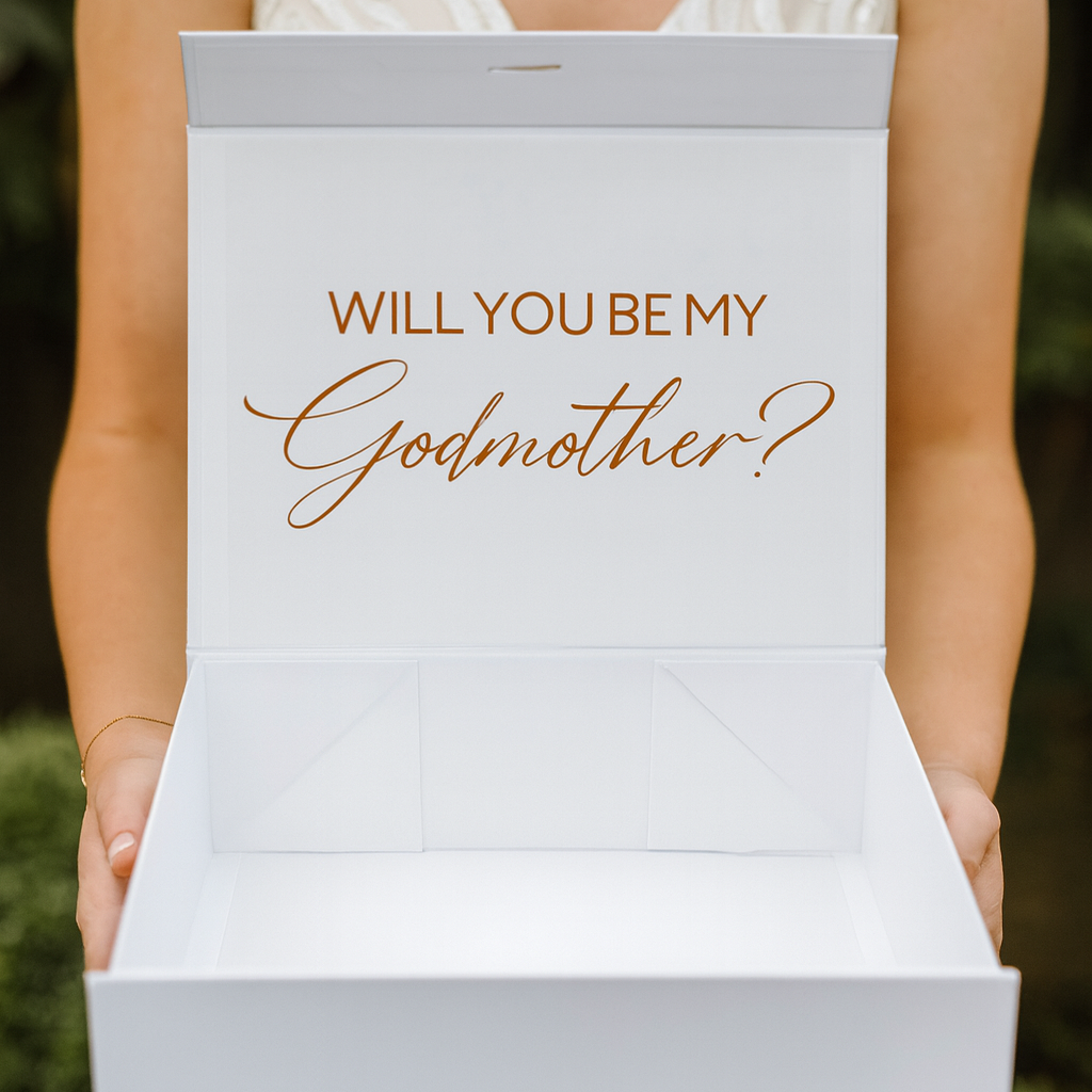 Person holding a box with 'Will You Be My Godmother?' text.