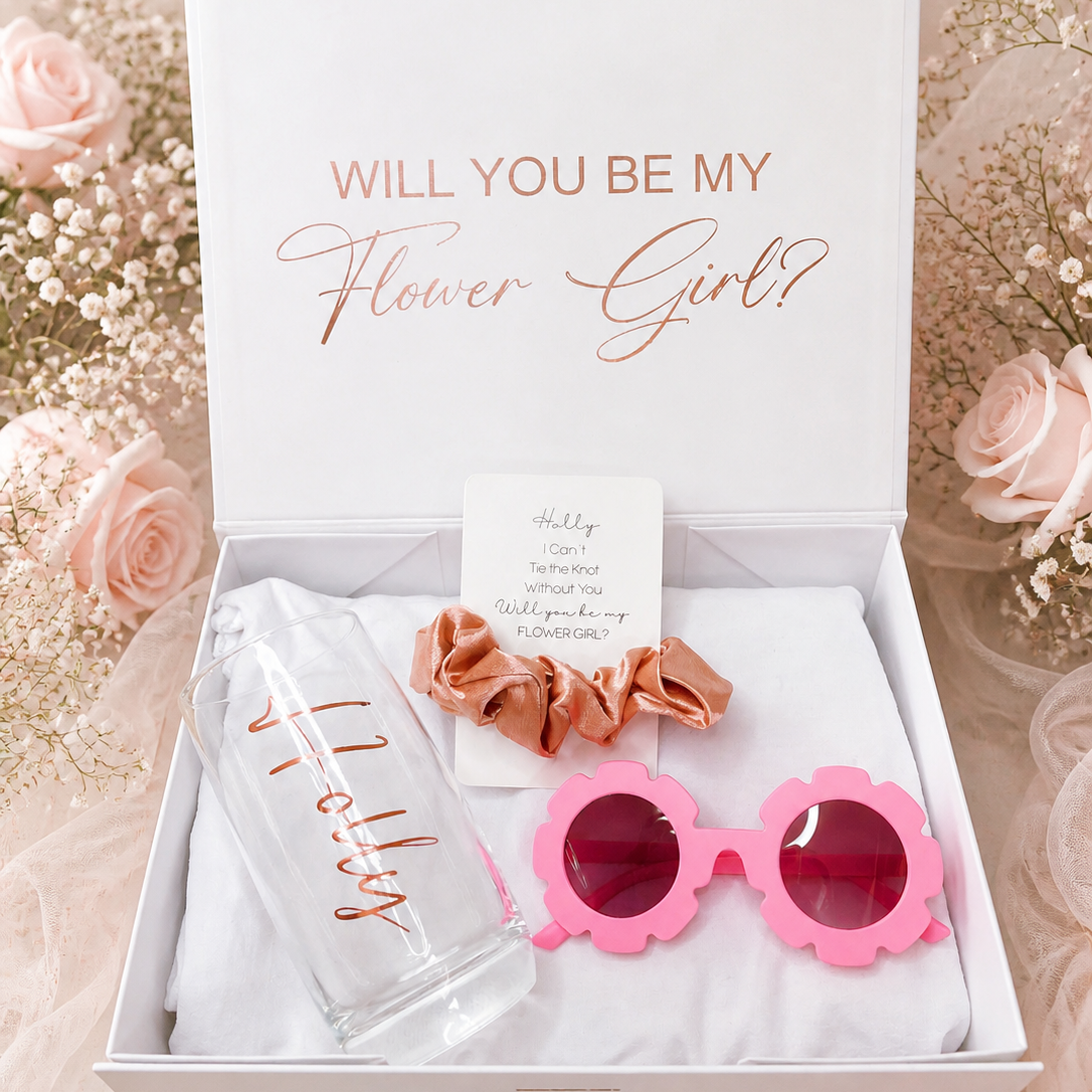 Gift set with pink sunglasses, hair scrunchies, and card in a box with 'Will You Be My Flower Girl?' text.