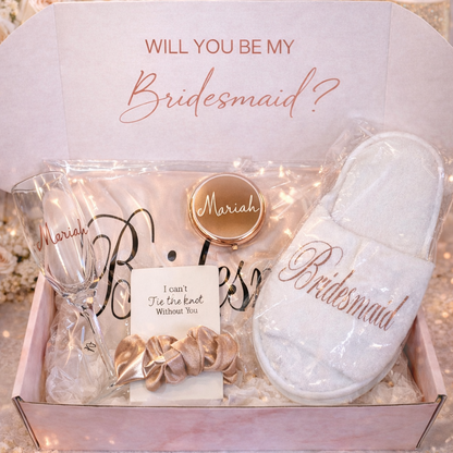 Bridesmaid proposal set with gift box, slippers, and champagne flute on a glittery background.