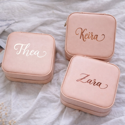 Three pink jewelry boxes with names 'Thea', 'Keira', and 'Zara' on a textured surface.