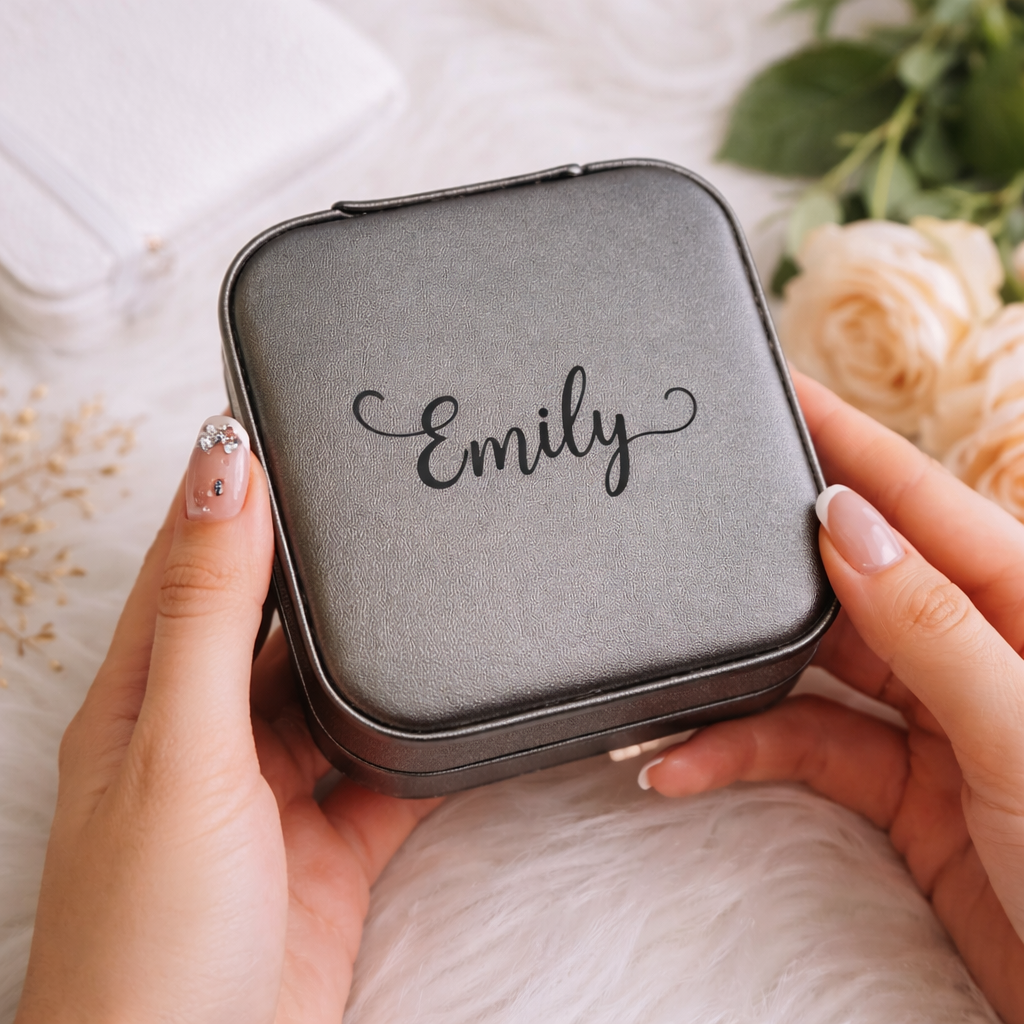 Person holding a small gray case with 'Emily' engraved on it, surrounded by flowers.