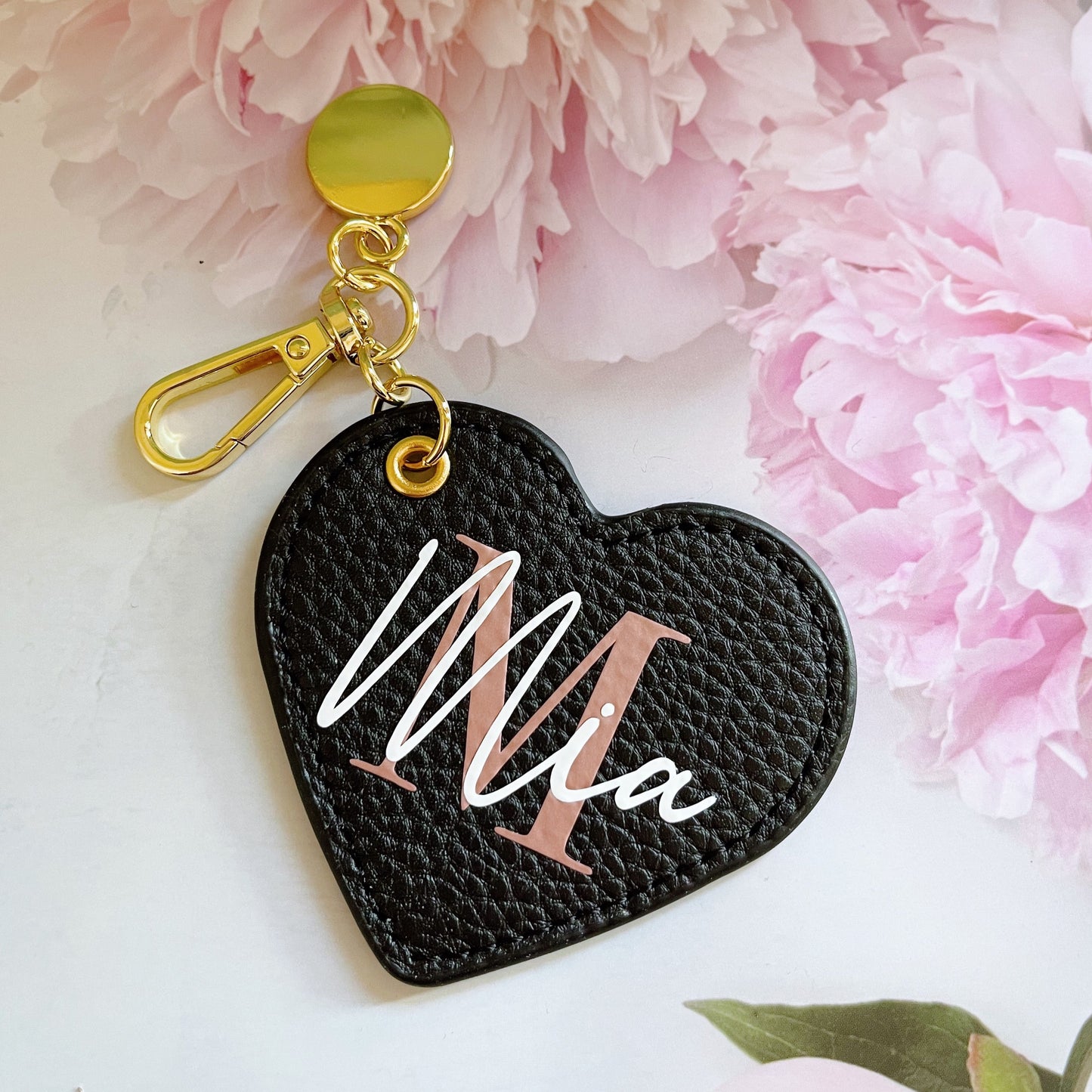 A heart-shaped keyring with the name 'Mia' inscribed on it, displayed against a floral background.